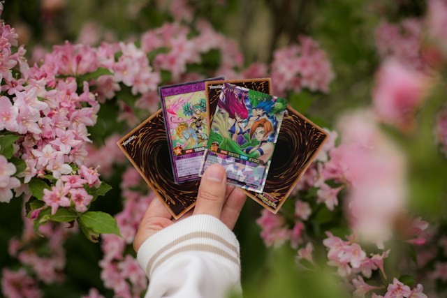 A hand holding Yu-Gi-Oh! Cards in front of flower blossoms